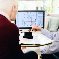 2 personnes jouent au sudoku avec le Télé-agrandisseur MagniLink One sur une table de salon