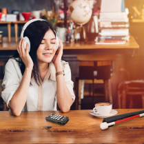 Lecteur audio et dictaphone Victor Reader Stream 3 utilisation par une femme avec un casque assise dans un café
