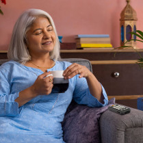 Une femme assise dans son canapé avec une boisson en train d'écouter le Lecteur audio et dictaphone Victor Reader Stream 3